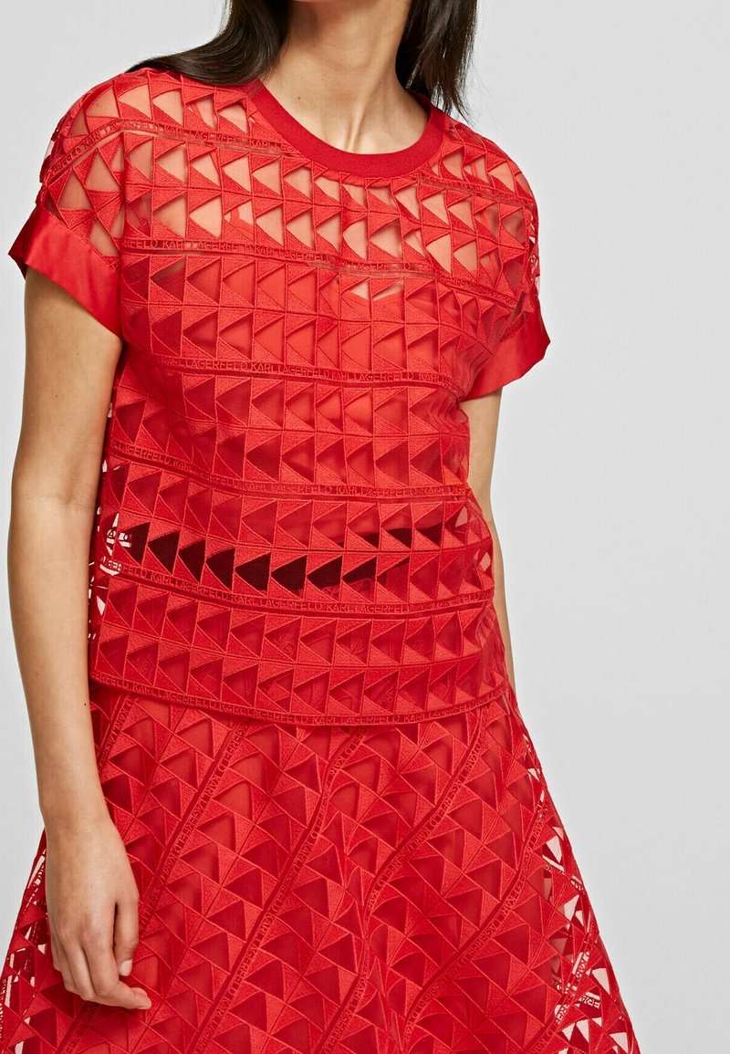 Top rojo de manga corta con un patrón geométrico de triángulos recortados. Fabricado con un tejido ligero y texturizado, con escote redondo.