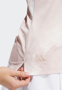 Lys pink træningstop i et blødt, tekstureret stof med en subtil gradient. Har et diskret beige logo og sideskår for bedre bevægelighed.