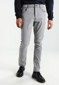 Pantaloni grigi in cotone misto con vestibilità slim, dotati di una vita standard, tasche frontali e una texture liscia, indossati con scarpe nere.