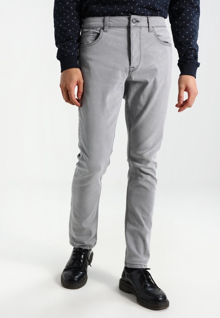 Pantaloni grigi in cotone misto con vestibilità slim, dotati di una vita standard, tasche frontali e una texture liscia, indossati con scarpe nere.