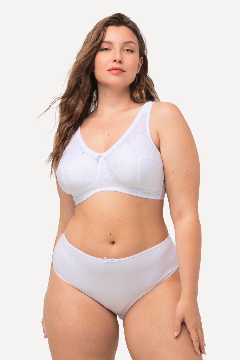 Donna con forme e lunghi capelli ondulati che indossa un reggiseno bianco di supporto con dettagli in pizzo e mutandine alte bianche abbinate, semplici.
