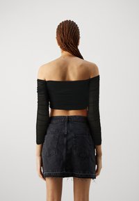 Must musta õlavarre pealt avatud crop top, millel on pikad, läbipaistvad varrukad, koos kõrge vöökohtadega musta denimpliidiga, millel on kulunud ääred ja tagakotid.