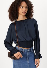Mornarji modra svila bluzica z nabranim vratnim izrezom in elastiko v pasu, dolgi rokavi z nabranimi manšetami, v kombinaciji z jeans krilom.