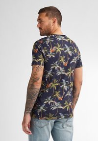 Tílko s krátkým rukávem v námořnické modři, zdobené živým potiskem palmy a kytary. Bavlněný materiál s volným střihem a kulatým výstřihem.