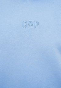 Ανοιχτό μπλε φούτερ από απαλό ύφασμα, με κεντημένο λογότυπο "GAP" σε ελαφρώς πιο σκούρο μπλε, στρογγυλή λαιμόκοψη και ομαλή υφή συνολικά.