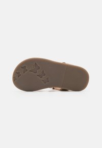 Semelle de sandale beige clair avec un caoutchouc texturé présentant des motifs de papillons. La semelle a un design plat avec des stries pour l'adhérence.
