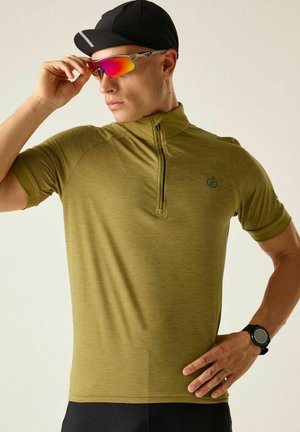 Man draagt een olijfgroen kortermig shirt met rits, zwarte pet, reflecterende sportzonnebril en zwart polshorloge, past zonnebril met hand aan.
