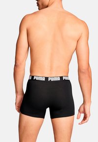 Schwarze Boxer-Shorts mit einem weißen, kontrastierenden Bund, der das Puma-Logo trägt. Glatte Textur, eng anliegendes Design und mittellange Länge bis zur Mitte des Oberschenkels.