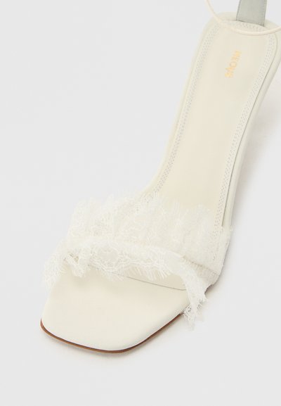 Λευκό σανδάλι με τετράγωνη μύτη, δερμάτινο λουράκι με δαντέλα και λεπτό κορδόνι στον αστράγαλο, με εσωτερική σόλα από λείο δέρμα και τη σφραγίδα "NEOUS".