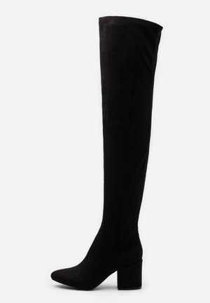 Botte noire mi-cuisses avec bout pointu et talon bloc épais, en matériau lisse semblable au daim, montrée de profil.