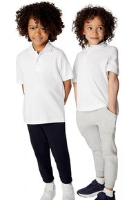 Dos niños están parados uno al lado del otro. Uno lleva una camiseta polo blanca y pantalones azul marino, el otro una camiseta polo blanca y pantalones deportivos grises.