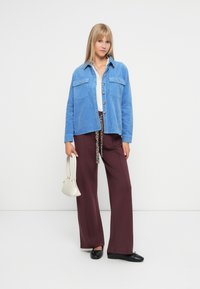 Ανοιχτό μπλε σακάκι από χοντρό ύφασμα με δύο τσέπες στο στήθος, συνδυασμένο με μπορντό παντελόνι φαρδιάς γραμμής και λευκό τοπ. Τα αξεσουάρ περιλαμβάνουν μια μικρή μπεζ τσάντα.