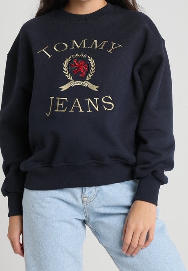 Marinblå sweatshirt i bomull med ett guldbroderat logotyp av "TOMMY JEANS" och en sköld med en röd lejon-design.