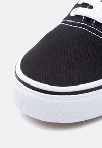 Μαύρο πάνινο αθλητικό παπούτσι με λευκά κορδόνια και λαστιχένια σόλα. Διαθέτει υφή λευκής μεσόσολας και αντιθετική μαύρη ραφή κατά μήκος της άκρης.