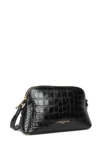 Sac en cuir noir embossé crocodile avec une fermeture éclair dorée, présentant un logo de marque doré à l'avant et une sangle ajustable pour le transport.