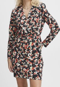 Robe à manches courtes présentant une base noire avec un motif floral abstrait coloré en rouge, blanc et vert. Tissu lisse avec un design enroulé.