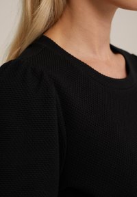 Pulover negru cu textură, cu decolteu rotund și mâneci bufante, evidențiind un model tricotat și un material neted.