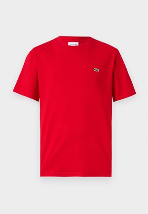 Tricou roșu din bumbac, cu mâneci scurte, guler rotund și un mic logo verde de crocodil pe partea stângă a pieptului. Textură netedă, croială casual.