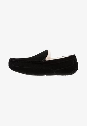 Black suede moccasin slipper with a soft cream lining, flat sole, and hand-stitched detailing along the seams.