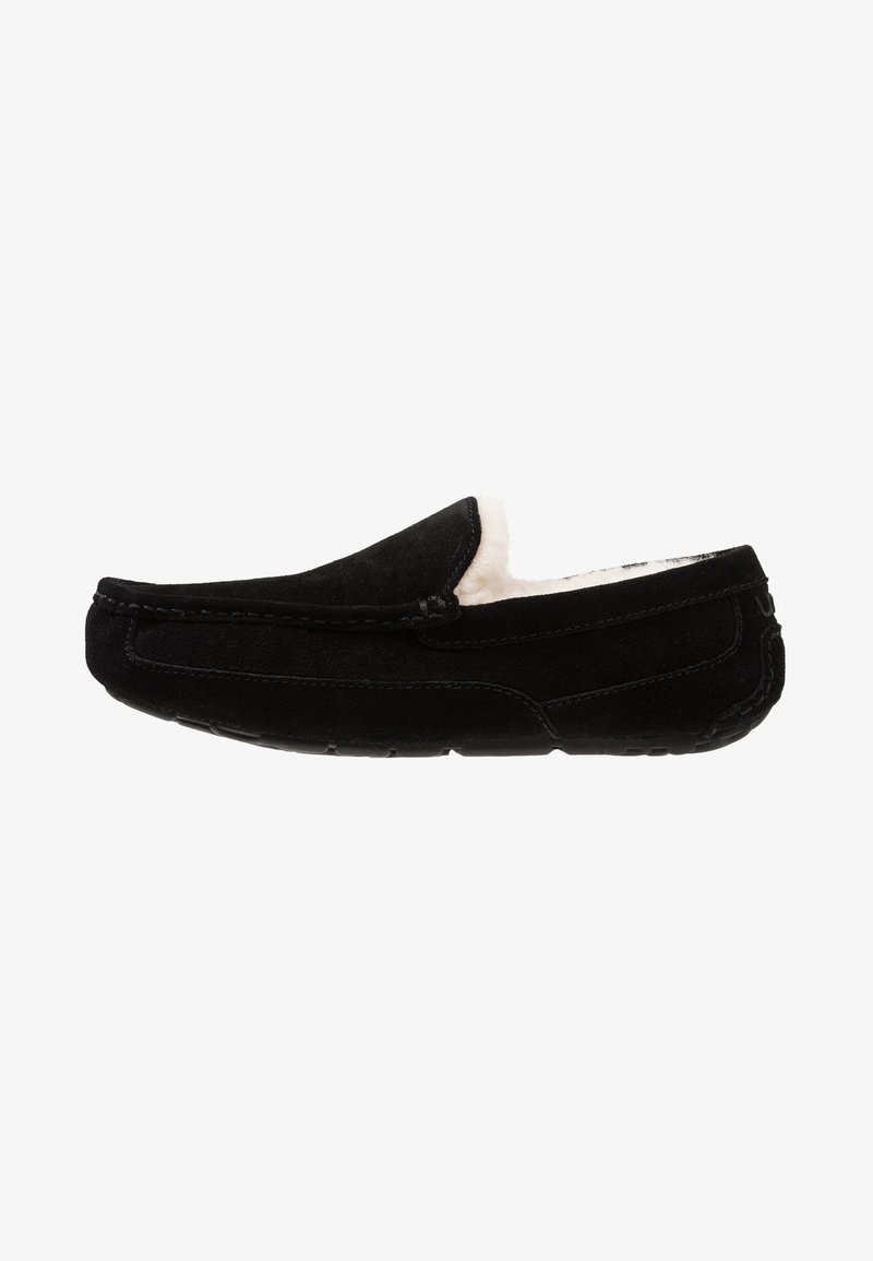 Black suede moccasin slipper with a soft cream lining, flat sole, and hand-stitched detailing along the seams.