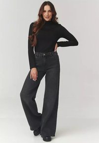 Czarny golf i czarne dżinsy z wysokim stanem i szerokimi nogawkami. Gładki materiał o luźnym kroju, z kieszeniami bocznymi i zapięciem na guzik.