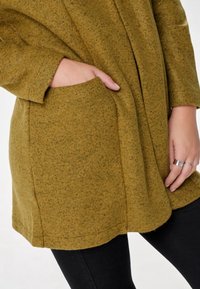 Olivgrön, texturerad kappa med långa ärmar och en framficka, med en avslappnad passform och ett mjukt, fluffigt material.