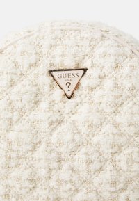 Borsa bianca trapuntata realizzata in tessuto testurizzato con accenti dorati. Presenta una piastra del logo Guess triangolare in marrone e crema.