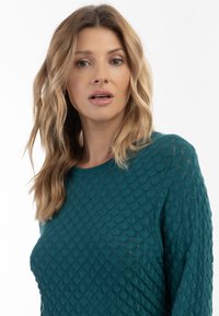 Maglione lavorato a maglia color teal con un design texturizzato a scaglie, scollatura rotonda e maniche lunghe. Tessuto leggero con una finitura liscia.