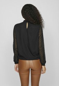 Black top with textured, sheer sleeves and a back keyhole. Paired with brown fitted pants featuring pockets and stitching accents.