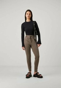 Black ribbed long-sleeve top, high-waisted beige trousers with drawstring, and black chunky sandals with studded accents.