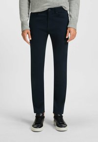Pantaloni slim-fit blu navy realizzati in morbido misto cotone, con un classico design a cinque tasche e chiusura con zip, abbinati a sneakers nere.