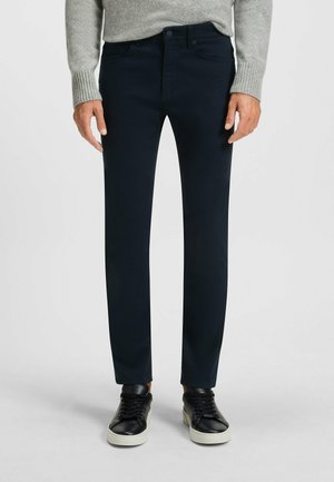 Marineblauwe slim-fit broek van een soepele katoenmix, met een klassieke vijf-pocket stijl en een rits, gecombineerd met zwarte sneakers.