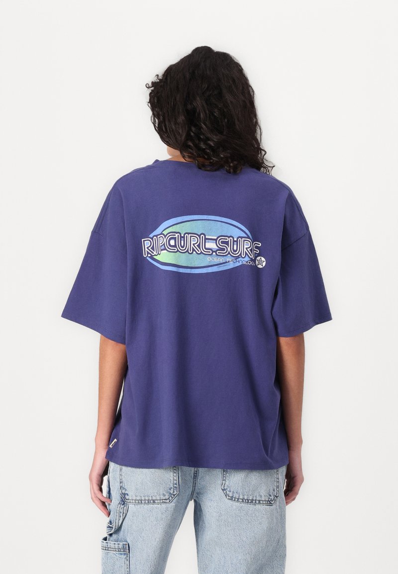 Fialová bavlnená tričko s veľkým, viacfarebným logom "RIPCURL-SURF" na chrbte. Krátke rukávy a voľný strih.