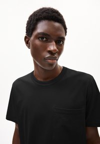 Zwarte katoenen T-shirt met een ronde halslijn en een linkerschouderzak, gladde textuur, korte mouwen en een losse pasvorm.