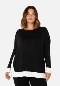 Black long-sleeve top with a rounded neckline and white hem accents. Soft fabric and relaxed fit with side slits. Classic color block design.