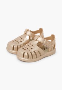 Light beige plastic sandals with a closed toe, woven strap design, and adjustable ankle strap. Slightly textured surface.