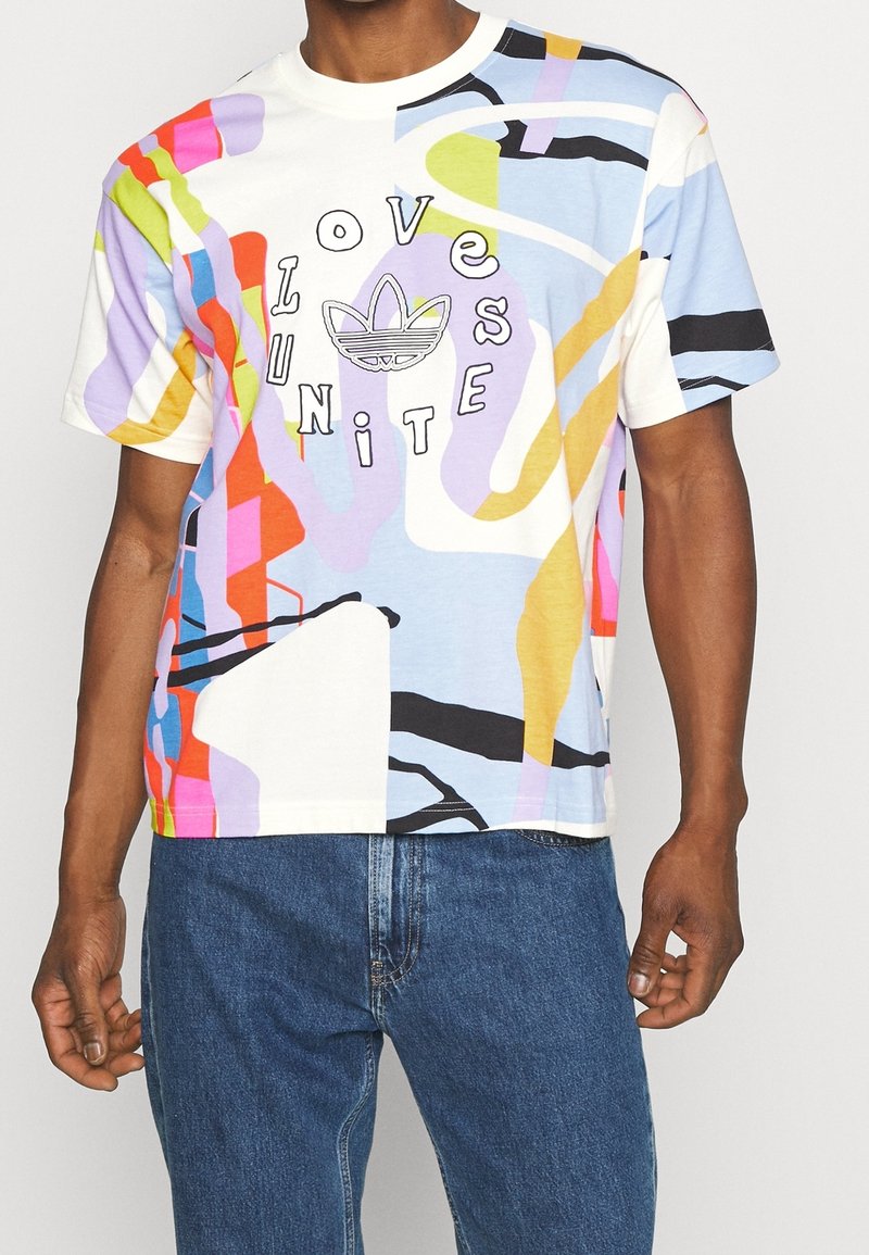 Kortärmad, flerfärgad t-shirt i bomull med grafisk design. Har djärva färger, abstrakta former och texten "LOVE UNITE" nära mitten.