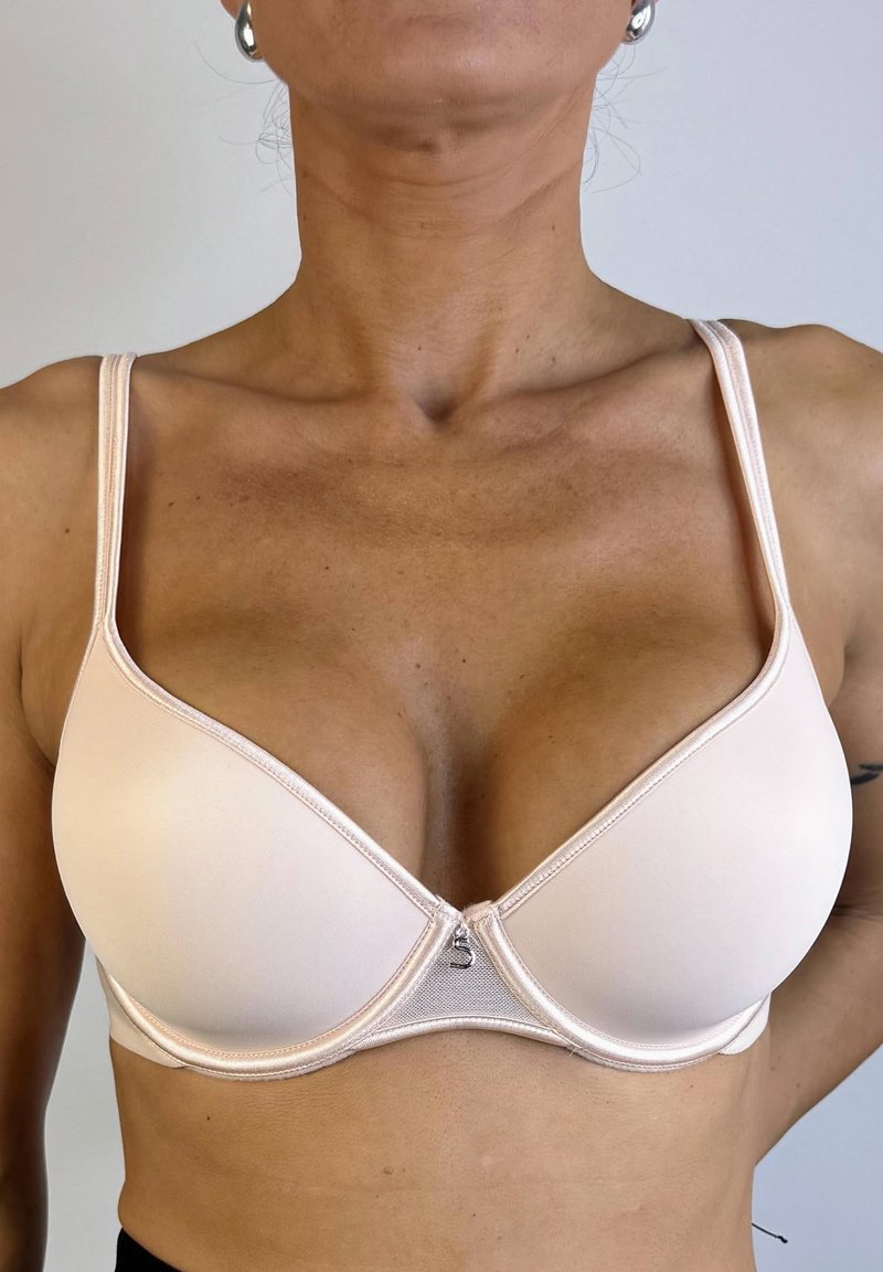 Sostén acolchado de color rosa claro con tirantes ajustables, textura suave y un pequeño detalle decorativo en el centro, que ofrece una forma moldeadora.