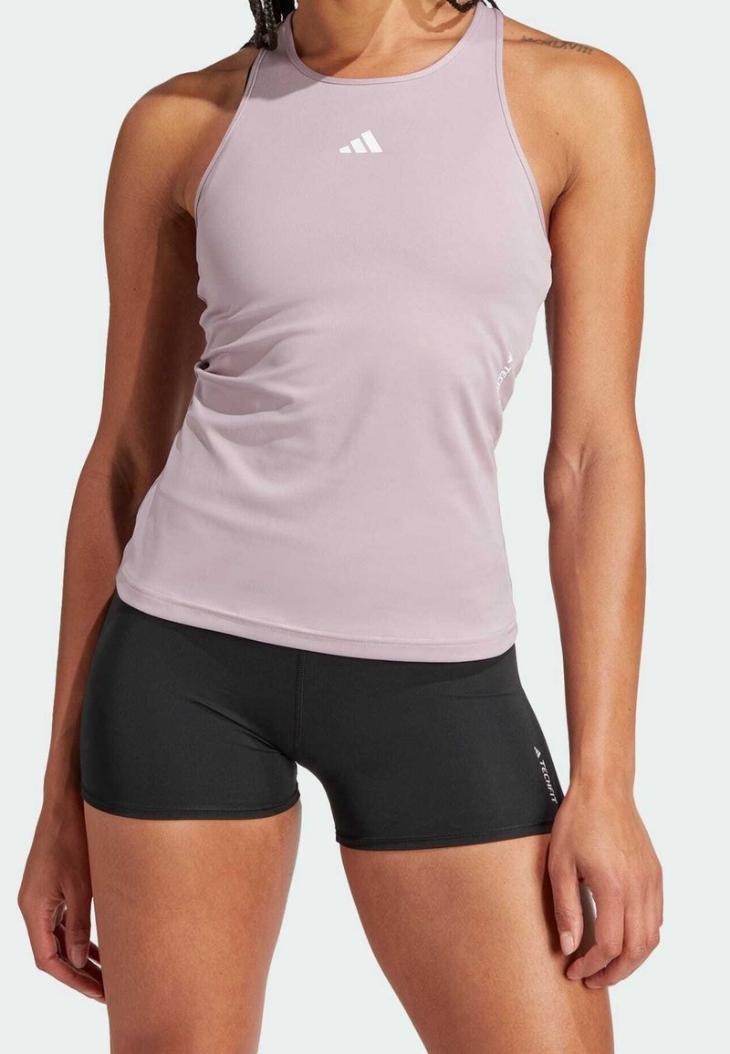 Top sportivo rosa chiaro con spalline sottili e un logo bianco, abbinato a pantaloni corti aderenti neri. Texture liscia e design attillato.