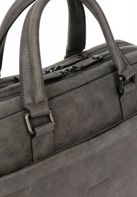 Valigetta in pelle grigia con doppi manici superiori, design strutturato, cerniere visibili e logo sulla parte anteriore. Presenta cuciture robuste e accessori metallici.
