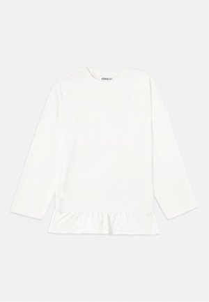 White long-sleeve top in soft fabric, featuring a ruffled hem. Its design includes a crew neckline and subtle branding at the chest.