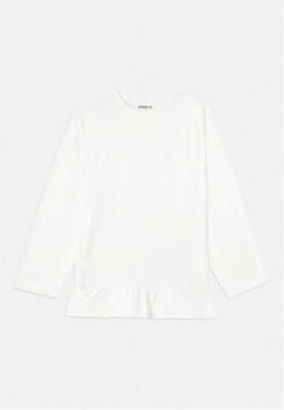 White long-sleeve top in soft fabric, featuring a ruffled hem. Its design includes a crew neckline and subtle branding at the chest.