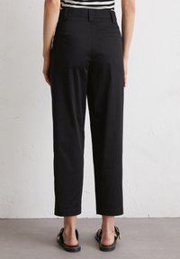 Zwarte broek van lichtgewicht stof, met een hoge taille, rechte pijpen en zijzakken. Draagt met casual sandalen.