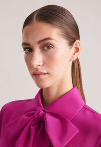 Blusa fucsia con un grande colletto a fiocco, realizzata in tessuto liscio, con un colletto strutturato e una vestibilità sartoriale.