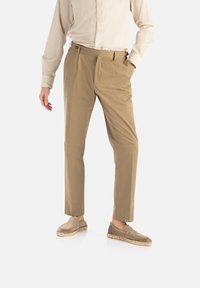 Beige skræddersyede bukser i et glat stof, med frontfolder og sidelommer, parret med lysebrune loafers med vævede kanter.