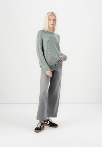 Lys grønn, strikket genser med bølgemønster, kombinert med høyt liv, vide grå jeans og svarte sneakers med brune detaljer.