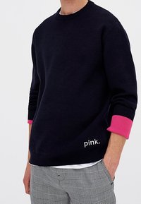 Maglione a collo rotondo navy con polsini rosa, con la parola "pink" ricamata in bianco. Materiale morbido, vestibilità comoda, abbinato a pantaloni a fantasia.