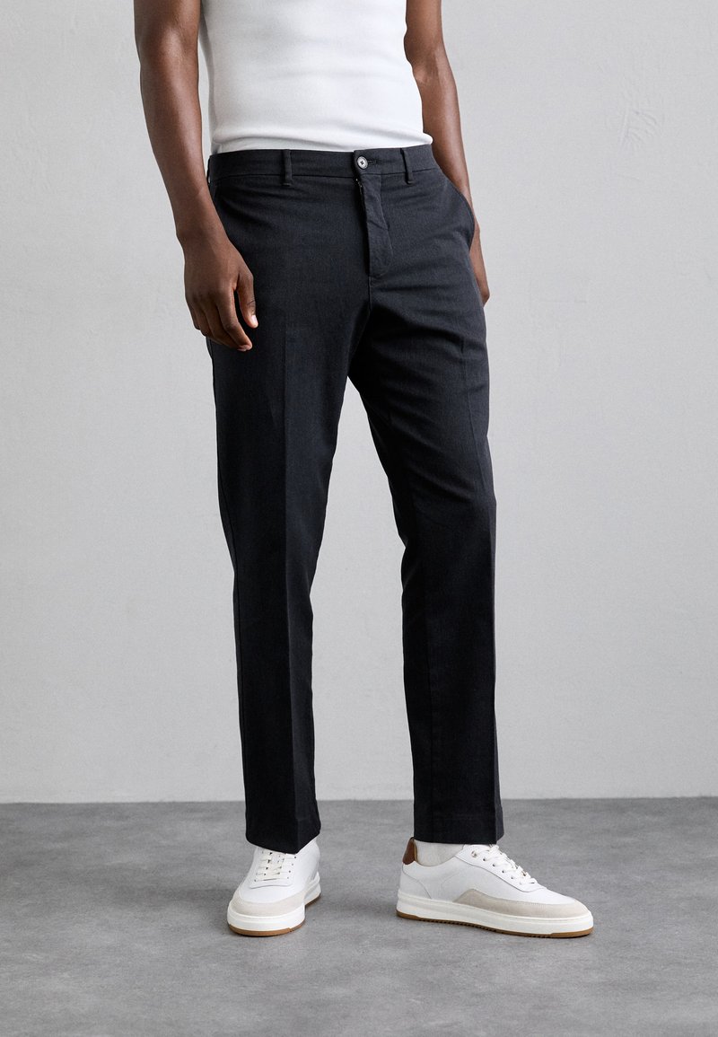 Mörkgrå, skräddarsydda byxor med rak bendesign, en enkel knappstängning och sidofickor, parat med vita sneakers.