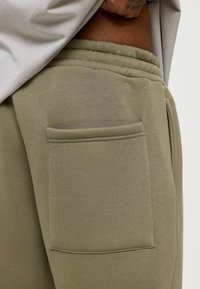 Olijfgroene jogpants met een gestructureerde afwerking, voorzien van een opgestikte zak aan de zijkant, een elastische tailleband en zachte stof.