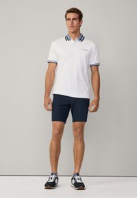 Bílá polokošile s límečkem a manžetami v námořnické modři, spárovaná s námořnickými šortkami a tmavými teniskami. Jednoduchý design s malým logem na košili.